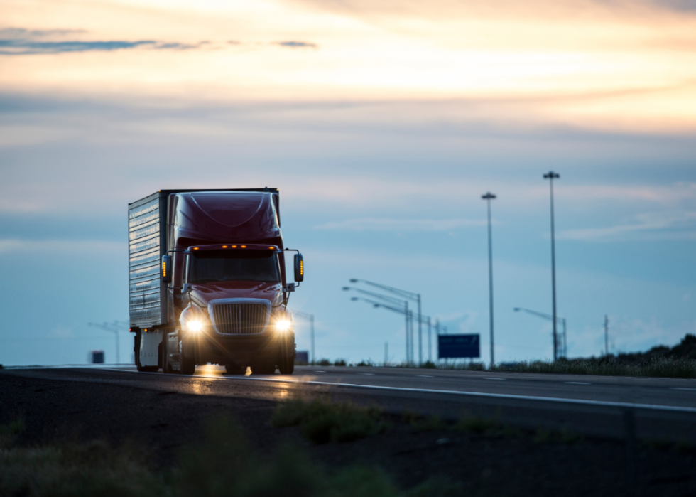 A large semi truck drives along a highway at susnset