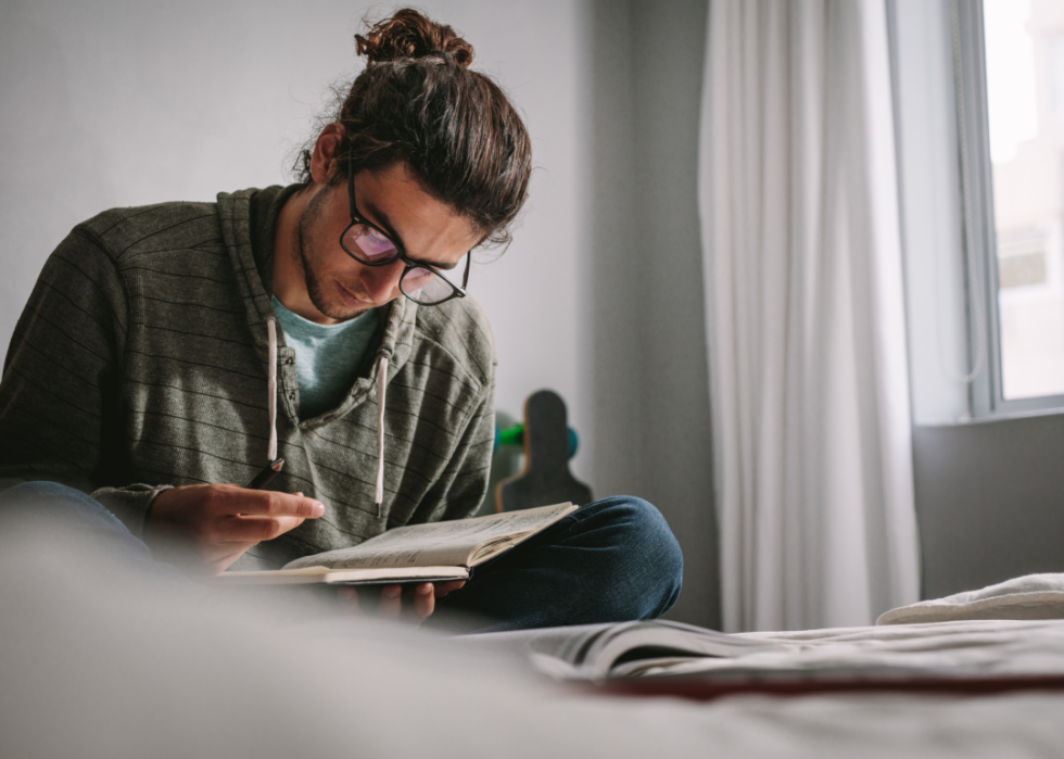 Male student reading from notebook at home