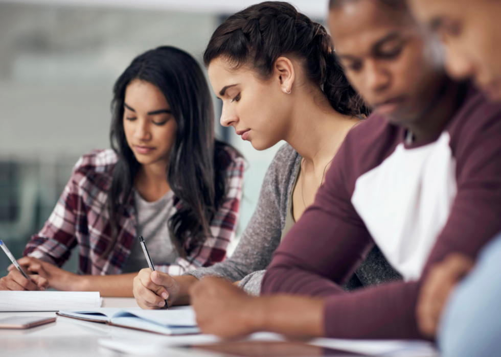 Four seated teen students writing in class