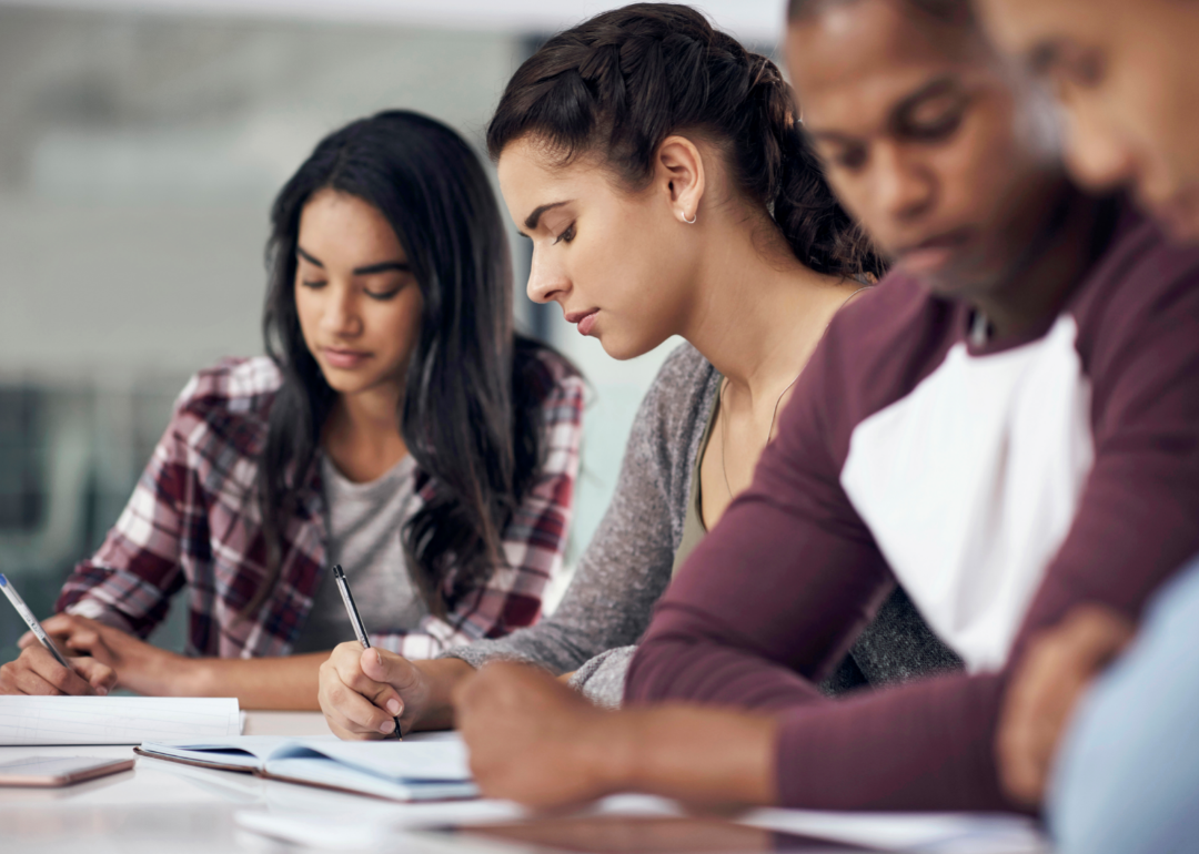 Four seated teen students writing in class.