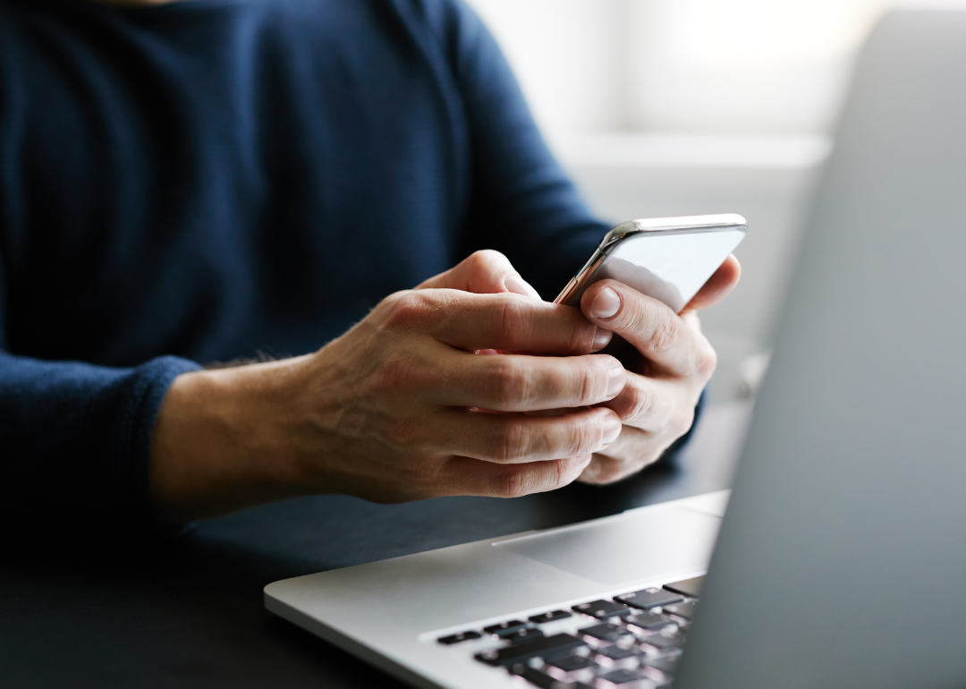 Person holding phone with open laptop.