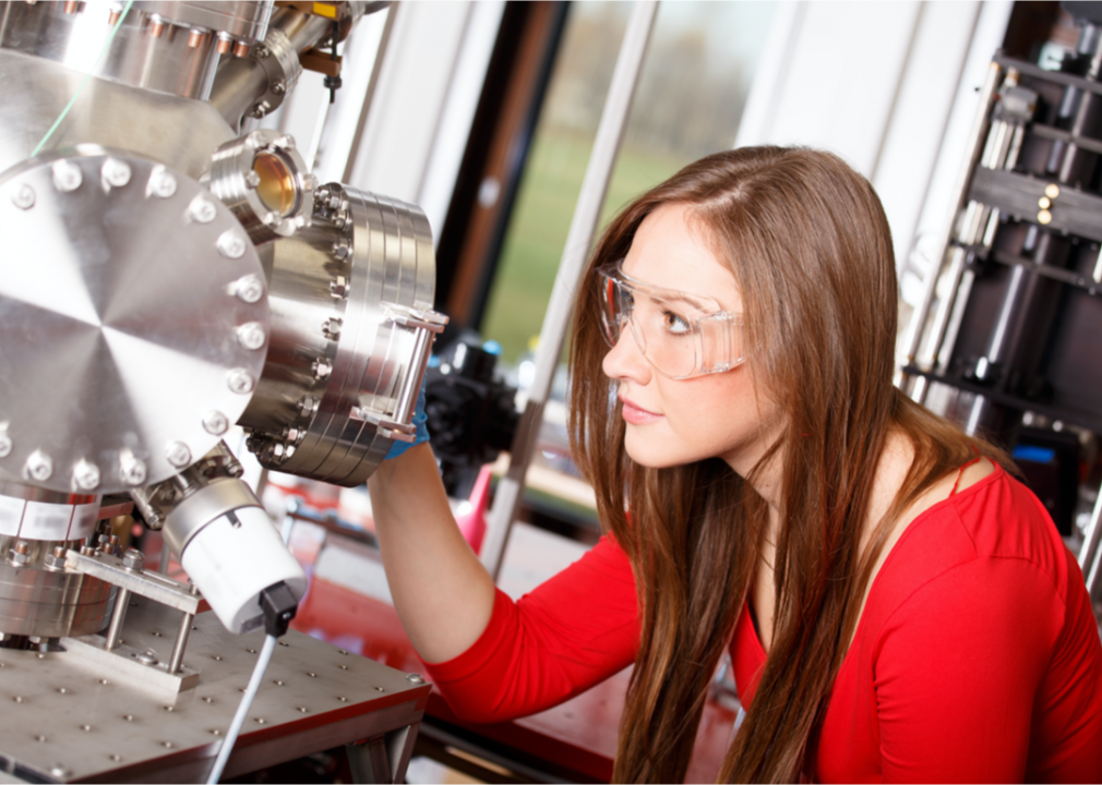 Woman physicist wearing safety goggles while looking into a microscope.