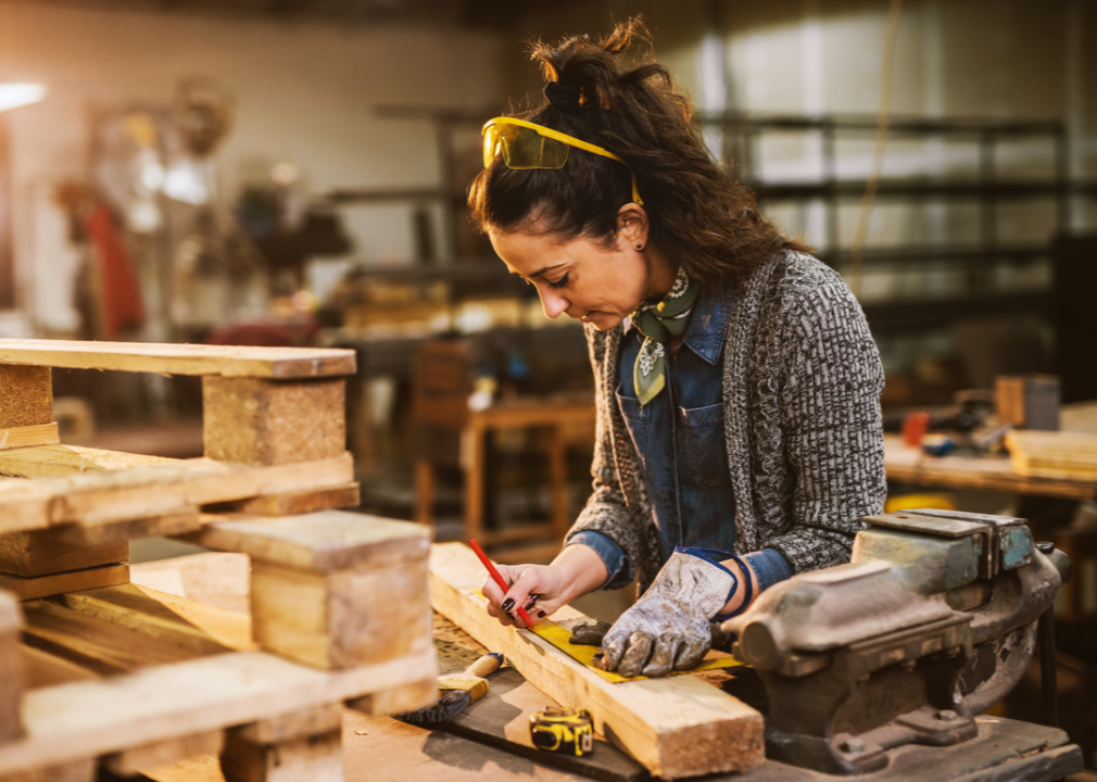 A worker makes a measurement on a piece of wood.