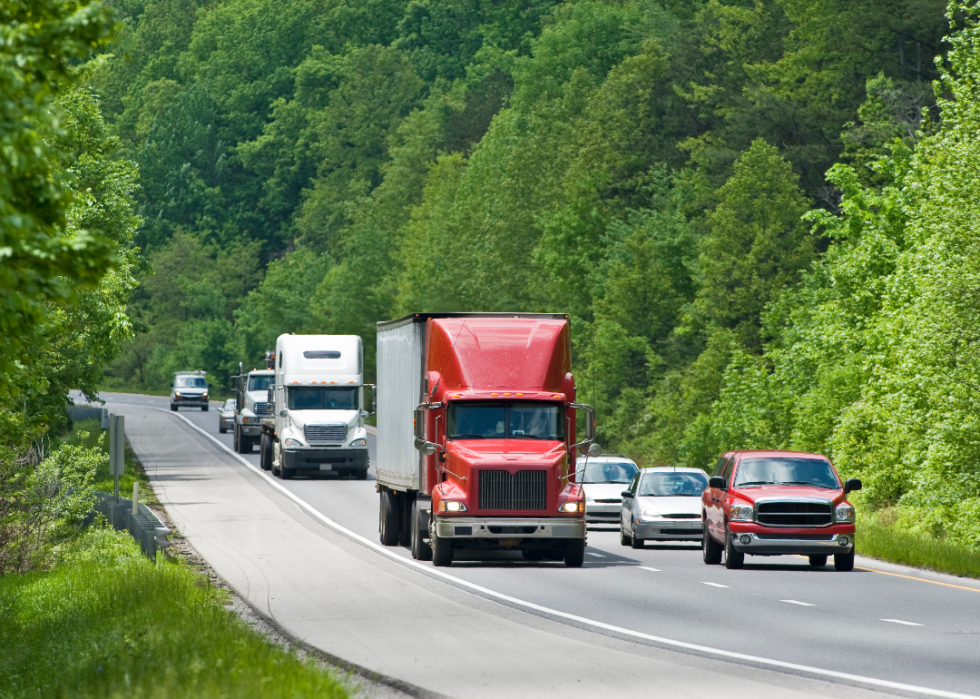 Two semi trucks drive along a winding road through a forest