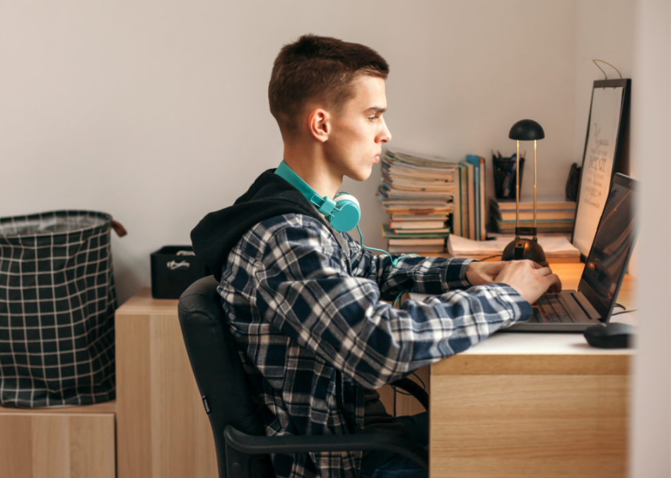 A teen sits at a desk staring intently at a screen.