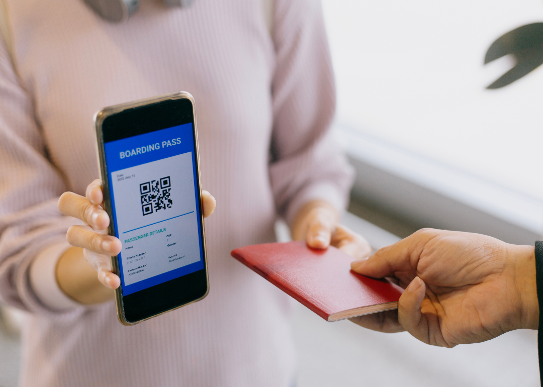 A person holding up a phone with a mobile boarding pass, handing someone a passport.