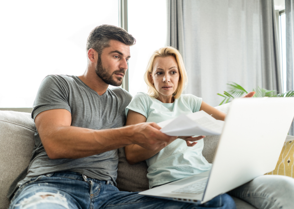 A couple looking anxious as they sit in front of the computer, managing their bills. 