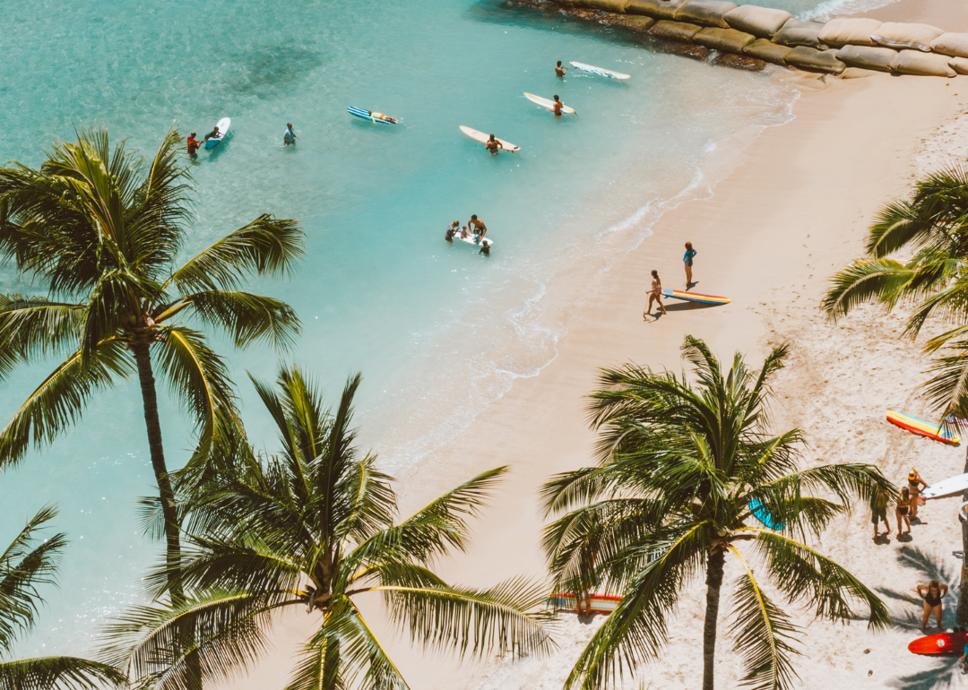 People with surfboards in the clear blue water on the beach.
