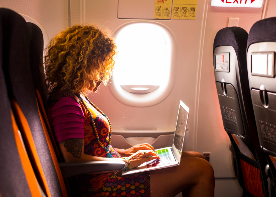 A woman types on her laptop on an airplane.