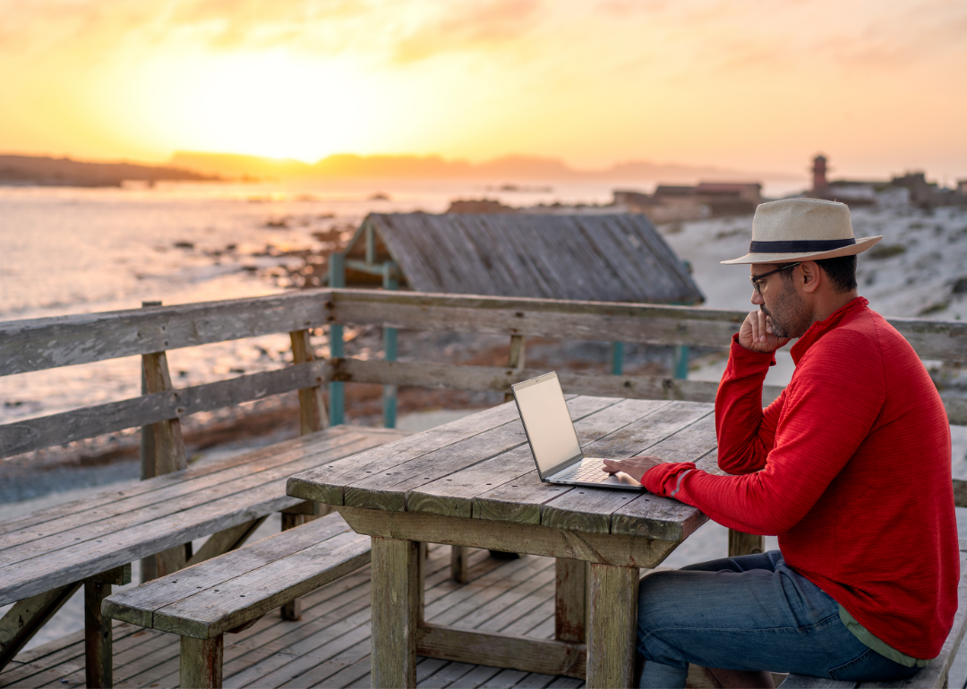 A man sits at a wooden table on a deck watching the sunset.