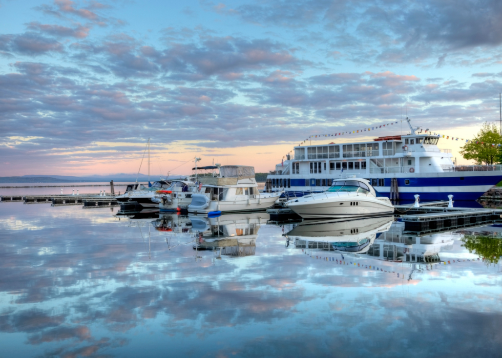 A harbor at sunset; in the foreground, there are several docked boats varying in size and style.