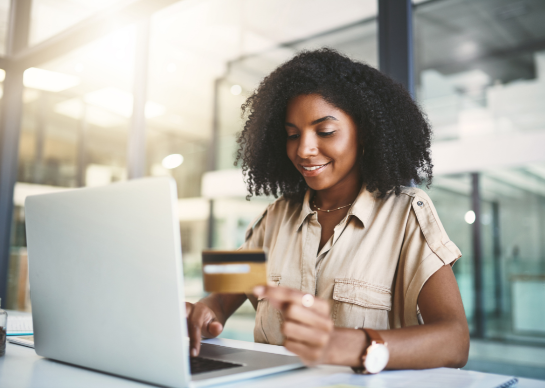 A woman sitting at a laptop with a gold credit card.