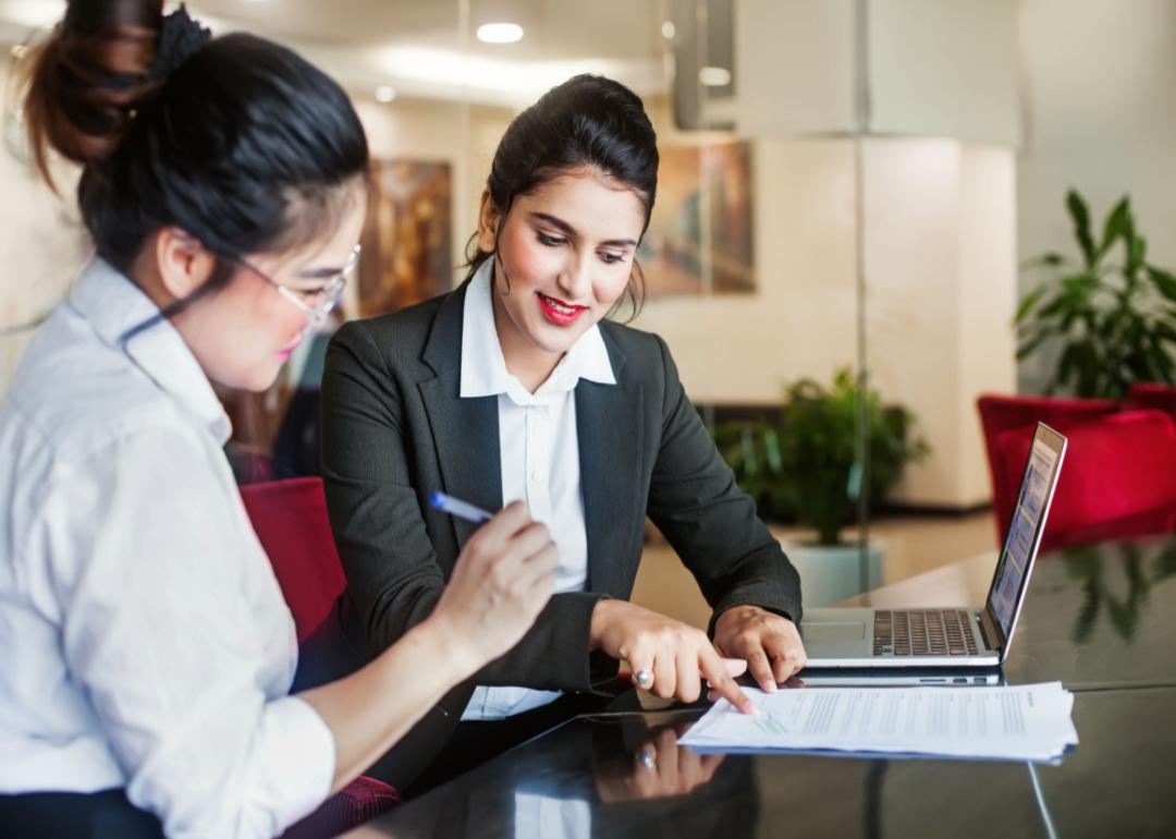 A woman signing paperwork with a professional woman at a desk.