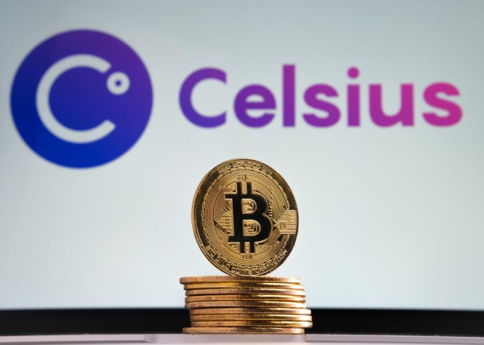 A gold bitcoin standing upright on a stack of other gold coins against a background of the Celsius logo.