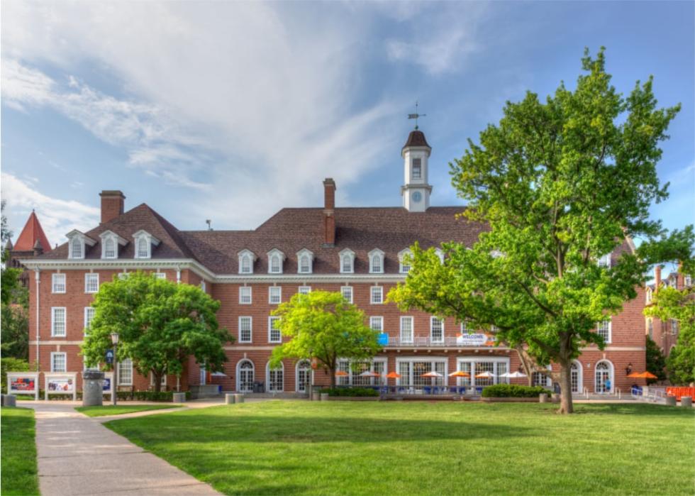 A red brick building with white tower with grass and trees in the foreground.