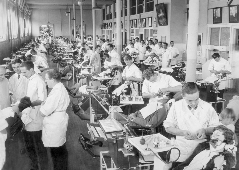 A large dentist hall with patients being qworked on in many rows of treatment chairs