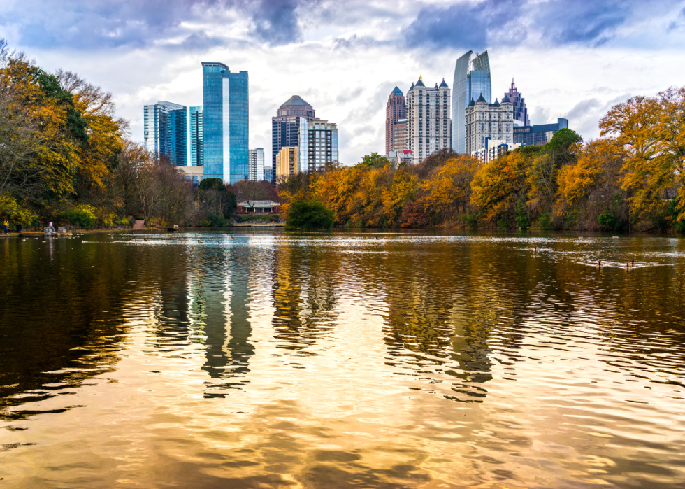 Skyscrapers by the body of water surrounded by trees in fall.