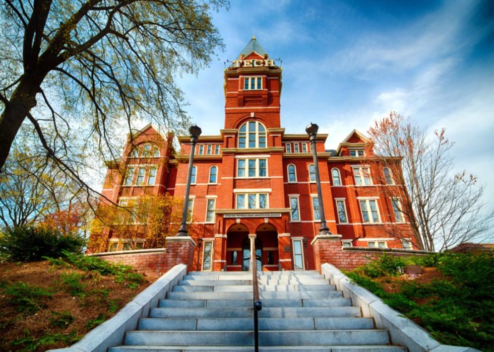 A red brick building with a tall tower in the center and concrete stairs leading to it.