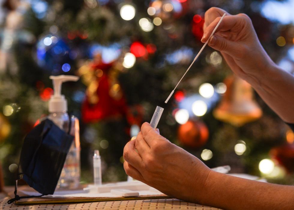 A person uses a COVID test with a Christmas tree in the background.