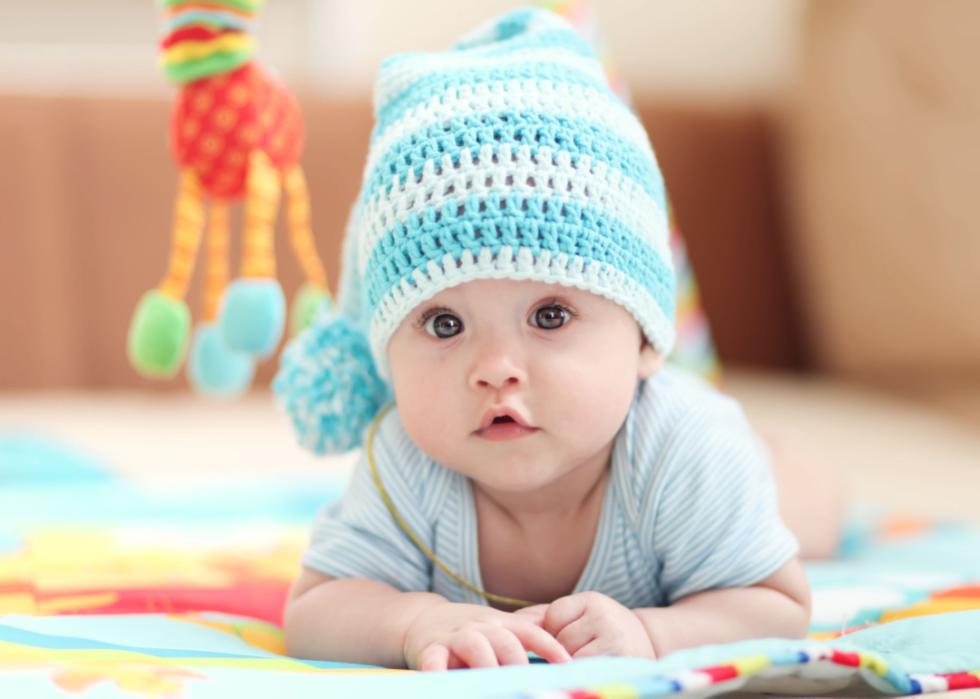 Baby girl lying on a children's rug in the white-blue cap.