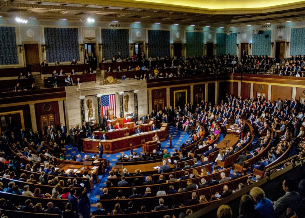 A number of people sitting in large room with wooden half circular benches.