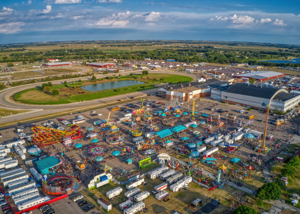 Aerial view of colorful rides with a large ferris wheel, RVs, and crowds of people attending state fair.