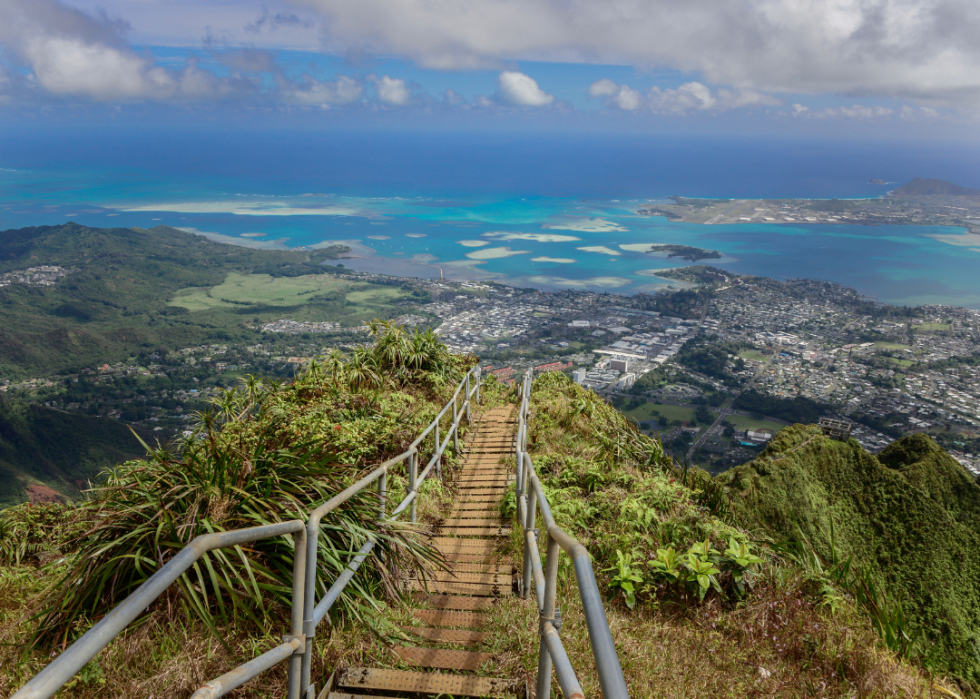 Stairs in the foreground with a town situated in a green valley surrounded by water and green mountains.