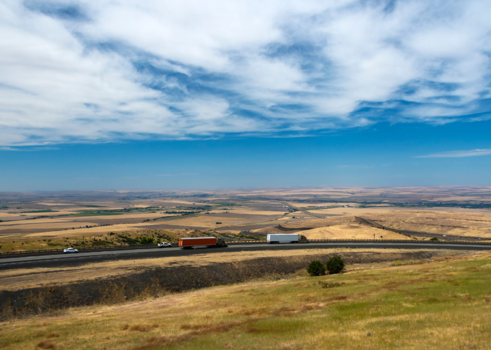 A few cars on a highway surrounded by yellow fields.