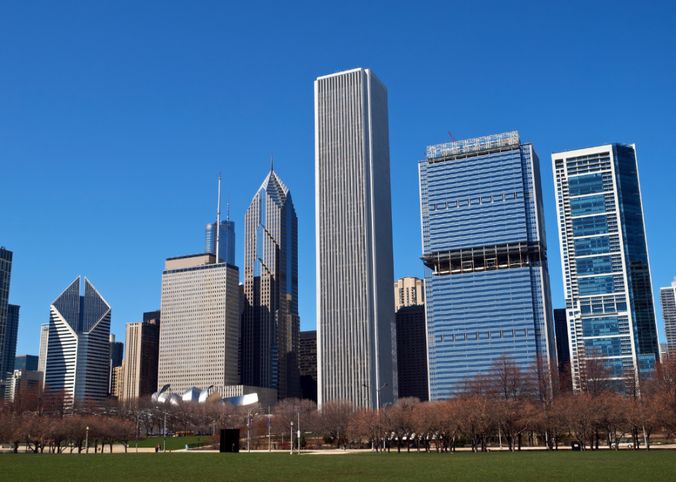 Modern steel and glass city skyscrapers by large field of grass in the foreground.