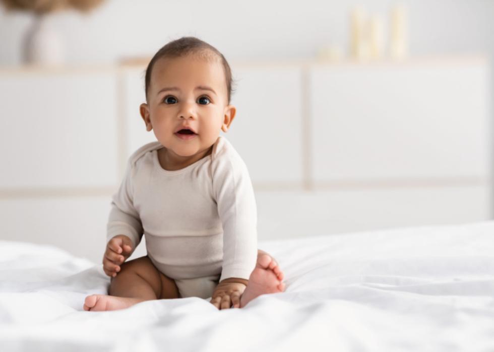 African American infant sitting on bed.