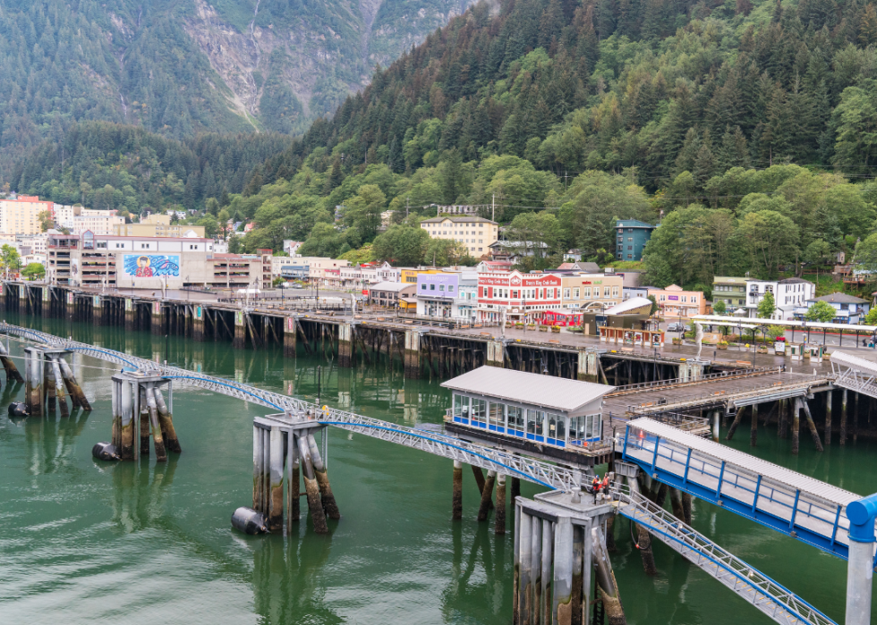 A row of buildings close to water with green mountains in the background.