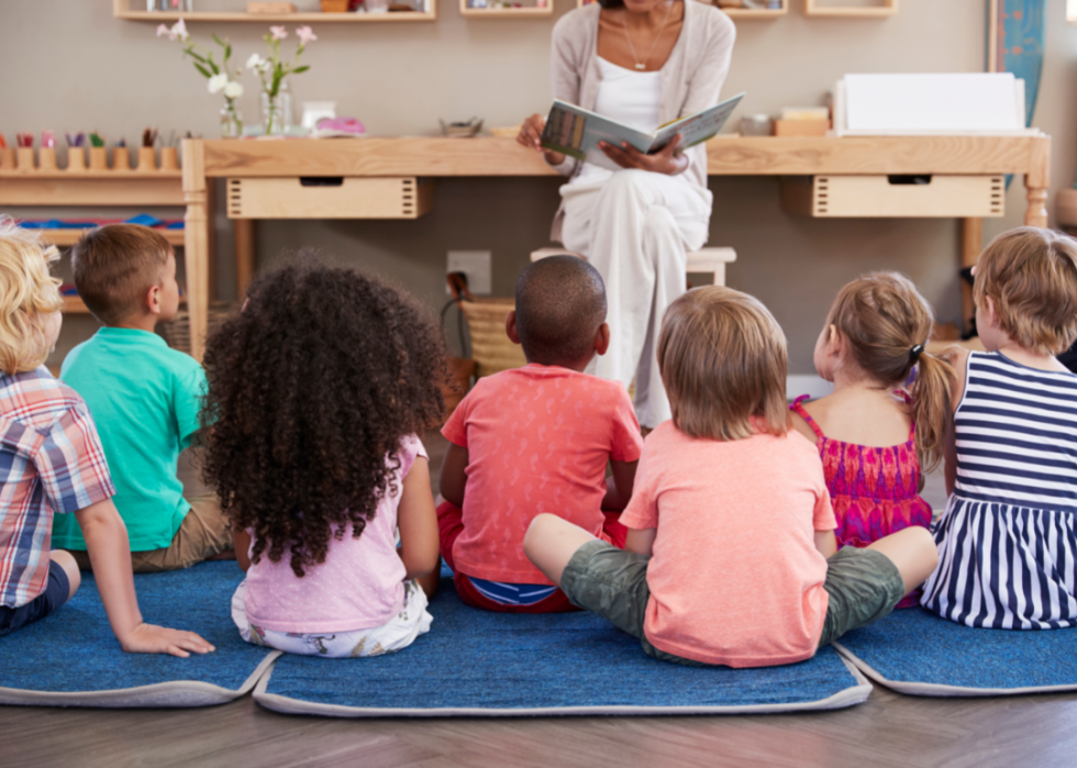 Young children sat on floor mats listening to their teacher read from a book.