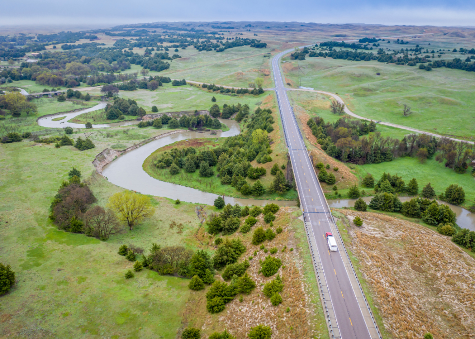 A highway in the middle of green fields and trees passing over a river.