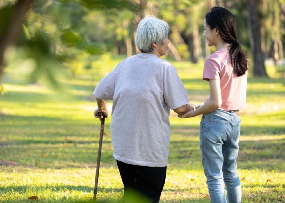 An older woman with a cane and a younger woman walking together in a park. 