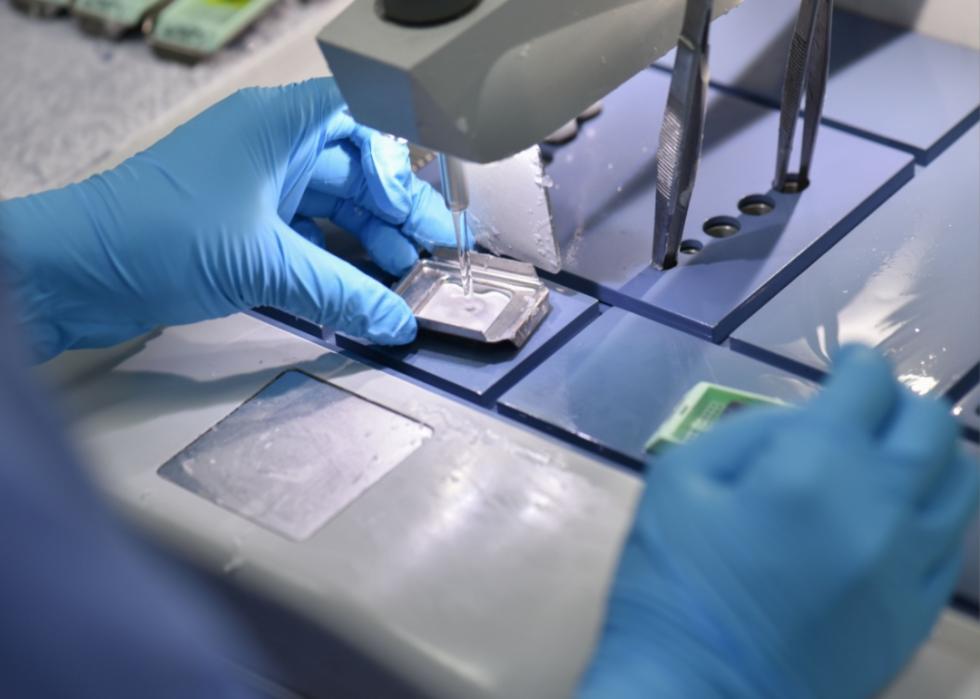 A pathologist in gloves testing a sample in a microscope.