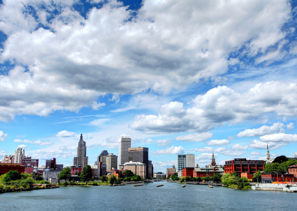 A city skyline with a river in the foreground and clouds in the background.