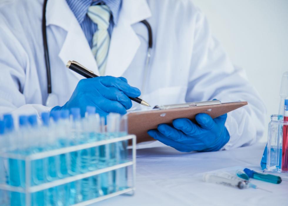 Medical researcher taking notes around vials.