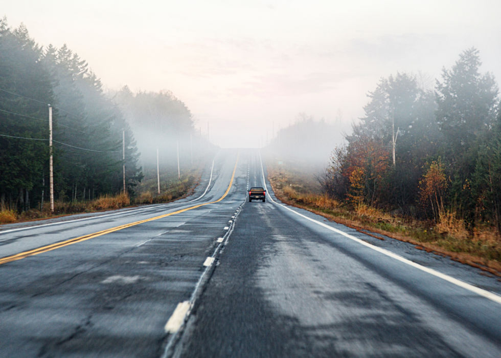 A pickup truck driving on foggy morning rural highway.