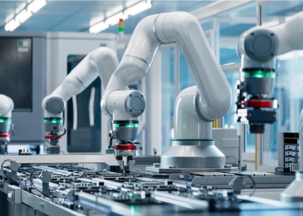A white robot arm inside bright electronics factory.