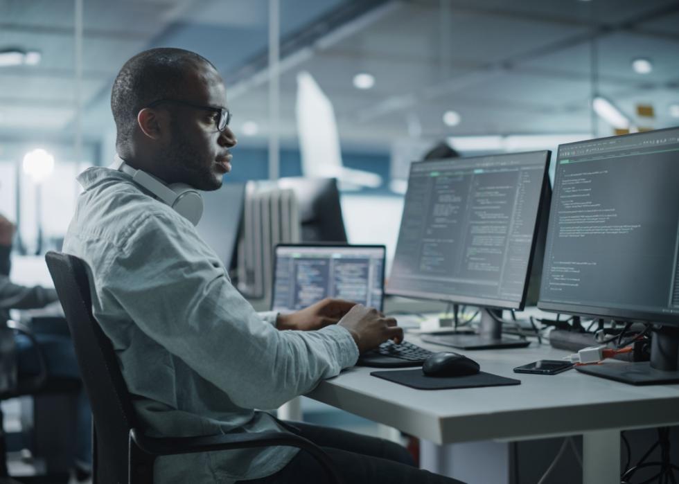 Black man working on desktop computer in a dimmed office.