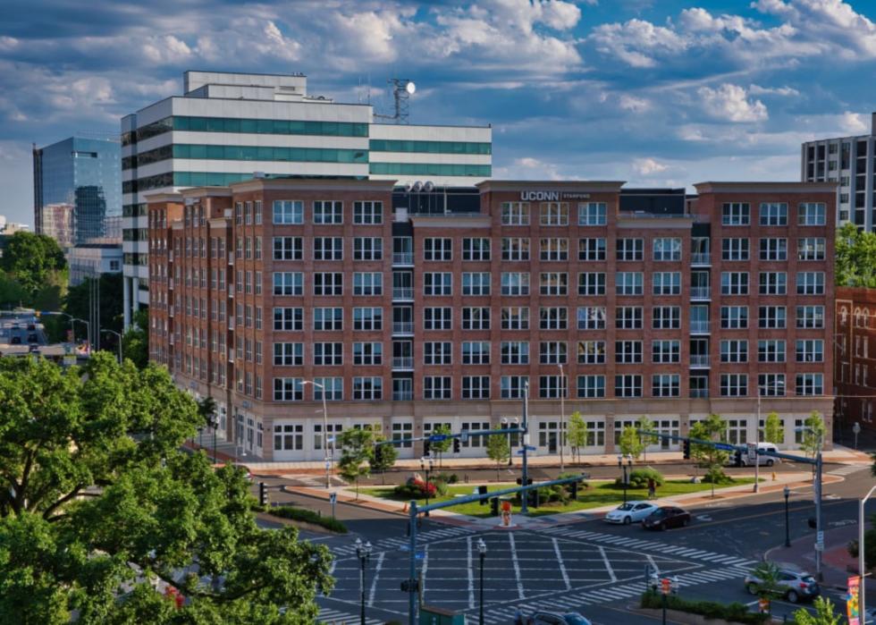 Modern brick building with lots of windows and sign saying UCONN on top and a parking lot in the foreground.