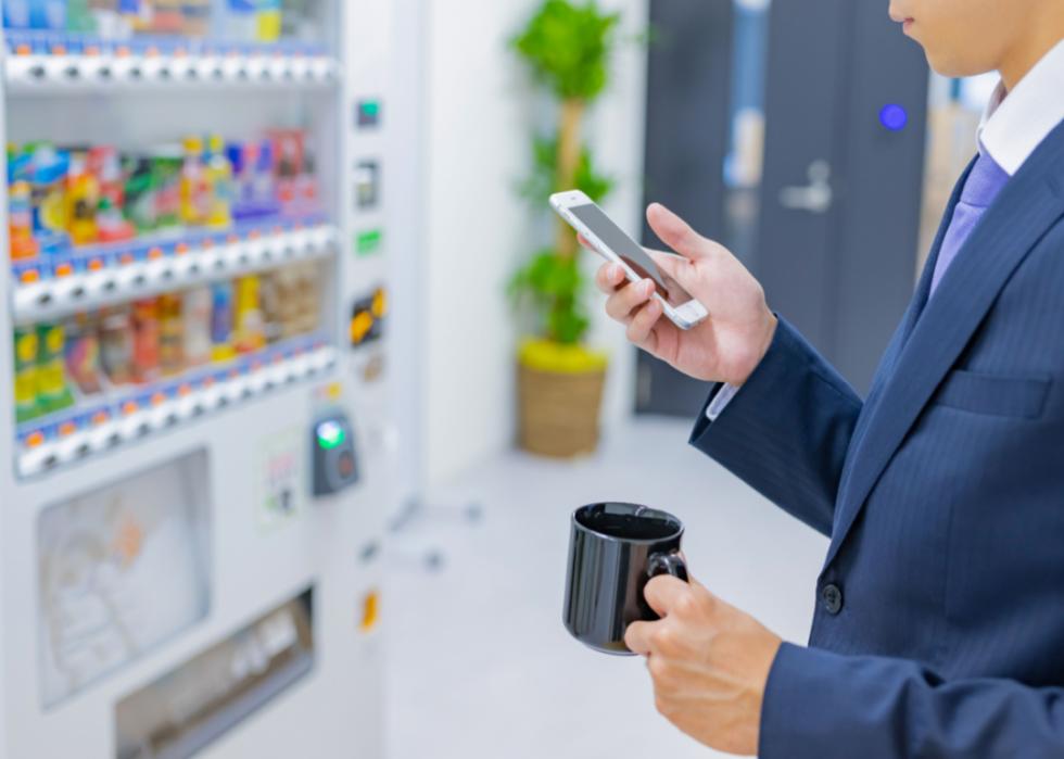 A person holding a cup of coffee in an office break room with snacks in the background.