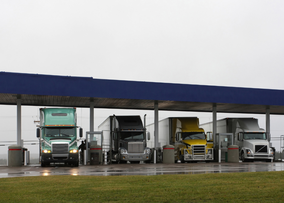 Four large trucks parked outdoors under the blue roof.