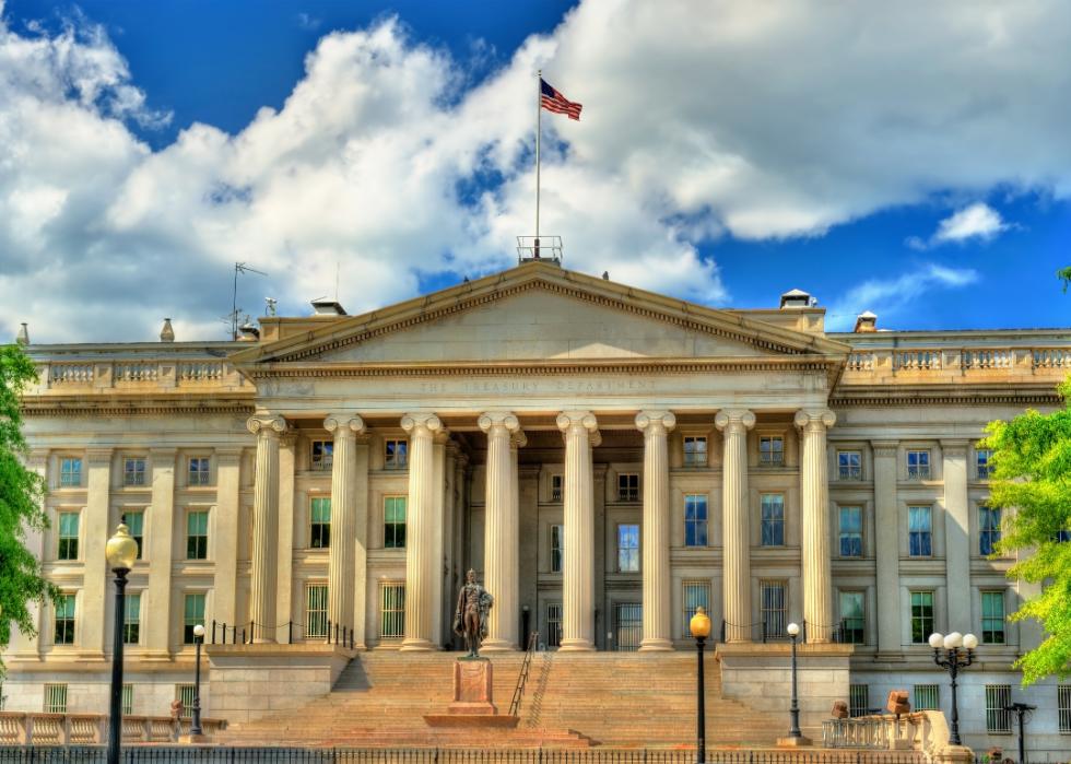 A large classical building made of limestone with a statue in front of it. 
