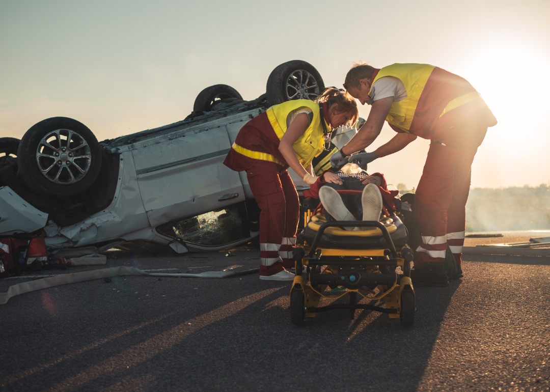 Paramedics helping a person on a stretcher after a car accident.