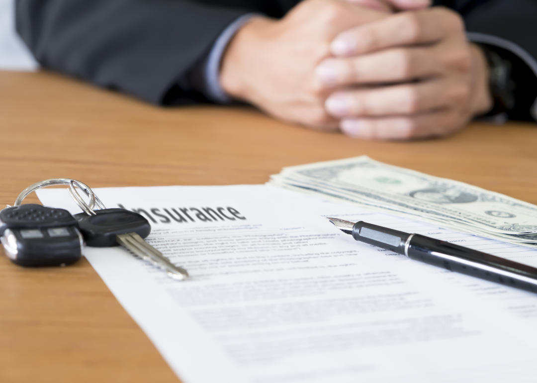 A car insurance document next to a set of keys and money to pay the premium.