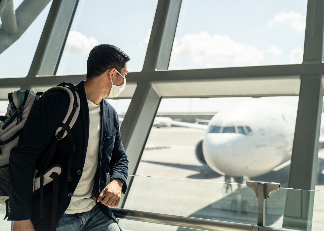 A person wearing face mask while waiting to board an airplane that is pictured in the background