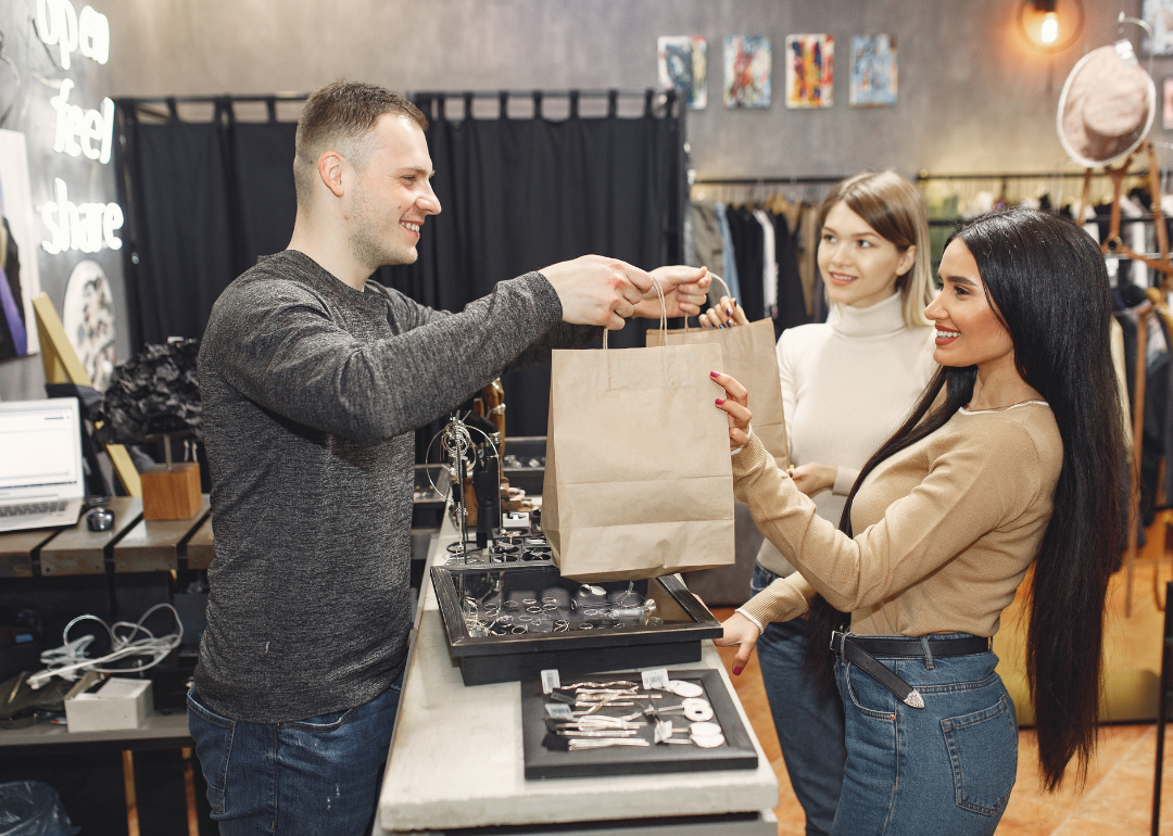 A worker handing paper bags to two customers.