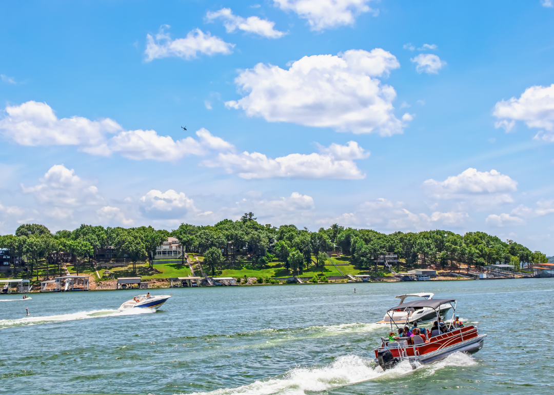 A pontoon boat full of people and two speedboats race on a lake in Oklahoma.