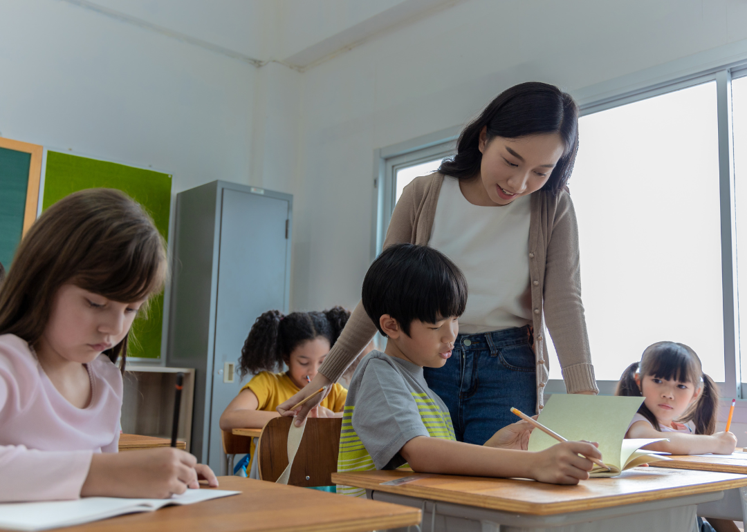 An elementary school teacher assisting a student at their desk